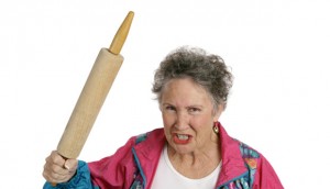A very angry senior lady holding a rolling pin and threatening to whack someone with it her husband Isolated on white